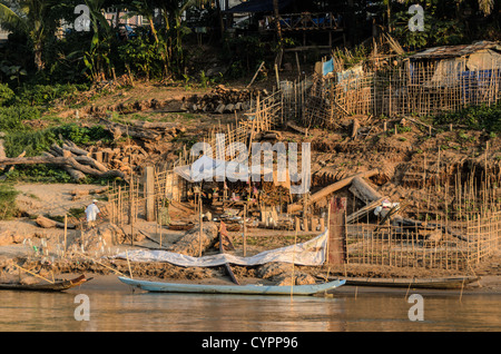 LUANG PRABANG, Laos — Ein einheimischer Landwirt bewirtschaftet einen kleinen provisorischen Bauernhof an den steilen, matschigen Ufern des Mekong-Flusses in der Nähe von Luang Prabang, Laos. Unter Ausnutzung der niedrigen Wasserstände der Trockenzeit nutzt der Landwirt das exponierte, fruchtbare Flussufer, um Nutzpflanzen anzubauen und traditionelle landwirtschaftliche Praktiken zu demonstrieren, die an die saisonalen Schwankungen des Mekong angepasst sind. Stockfoto