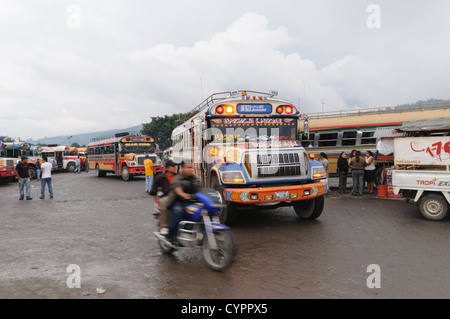 Huhn-Busse und ein Motorrad hinter dem Mercado Municipal (Stadtmarkt) in Antigua, Guatemala. Aus diesem umfangreichen zentralen Busbahnhof strahlenförmig der Routen in Guatemala. Oft bunt bemalt, die Huhn-Busse sind nachgerüsteten amerikanische Schulbusse und bieten ein günstiges Transportmittel im ganzen Land. Stockfoto