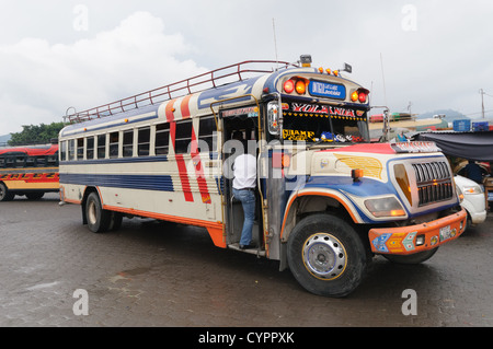 ANTIGUA GUATEMALA, Guatemala – Fahrt mit Hühnerbussen hinter dem Mercado Municipal (Stadtmarkt) in Antigua, Guatemala. Von diesem ausgedehnten zentralen Autobahnkreuz aus verlaufen die Routen quer durch Guatemala. Die oft bunt bemalten Hühnerbusse sind nachgerüstete amerikanische Schulbusse und bieten günstige Verkehrsmittel im ganzen Land. Stockfoto