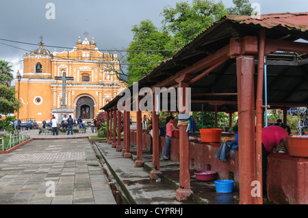 SAN PEDRO LAS HUERTAS, Guatemala – die gebrannte siennafarbene Iglesia en San Pedro las Huertas, etwa 15 Minuten von Antigua entfernt. Diese historische Kirche ist bekannt für ihre auffällige Farbe und die Kolonialarchitektur, was sie zu einem bemerkenswerten Wahrzeichen in der Region macht. Der gemeinschaftliche Wäschereibereich befindet sich auf der rechten Seite. Stockfoto