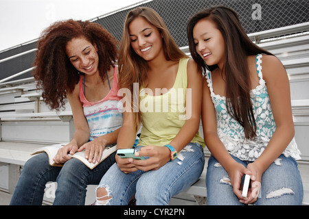 Schulfreunde sitzen zusammen auf der Tribüne Blick auf Handy Stockfoto