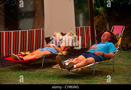 Ein paar Schlaf auf Sonnenliegen außerhalb der Markise den abgestellten Wohnwagen auf einem Campingplatz in Devon. Stockfoto