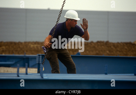 Ein Bauarbeiter hilft ein Kranführer senken oder heben Sie einen Stahl Gürtel auf einer Baustelle. Stockfoto