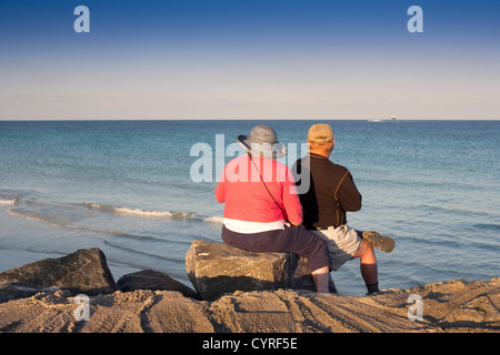 Ein älteres Paar mit Blick auf das Meer und genießen den Sonnenuntergang am Pointe Park Miami South Beach an einem Nachmittag im Dezember Stockfoto