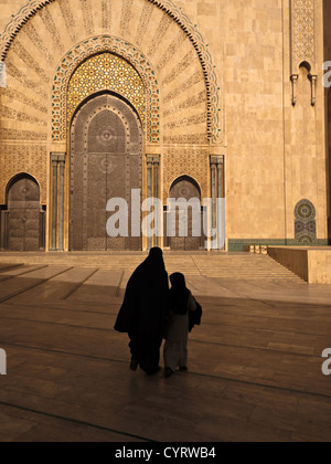 Silhouette einer Frau in traditioneller Kleidung Burka und weibliches Kind zu Fuß in Richtung Hassan-II.-Moschee in Casablanca, Marokko. Stockfoto