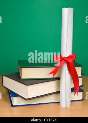 Ein Haufen Bücher und ein Diplom. Leere Tafel im Hintergrund. Stockfoto