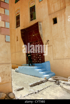 Junge stand auf der blauen Tür geschnitzte Holztür von einem in der Regel gestrichene Gebäude, Wadi Doan, Jemen Stockfoto