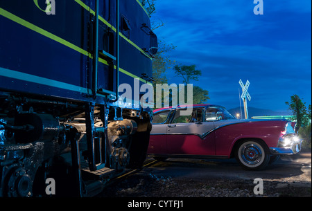 Blaue Zug Eisenbahn Dieselmotor trifft fast Oldtimer Thunderbird Auto am Bahnübergang in der Nacht Stockfoto