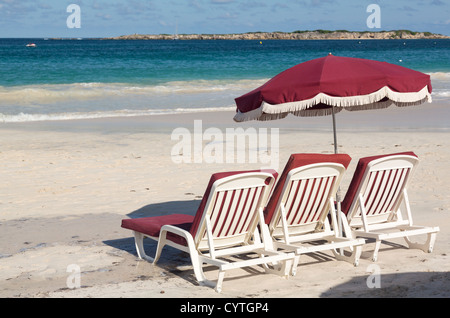 Drei weiße Kunststoff Strand Liegestühle und Sonnenschirm am Orient Beach St Martin Stockfoto