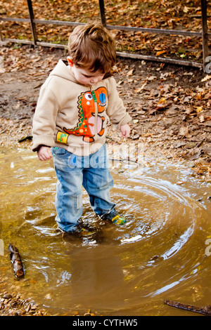 Ein junger Boy spritzt und spielt in einer schlammigen Pfütze auf dem Lande Stockfoto