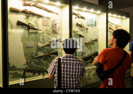 HO CHI MINH CITY, Vietnam - Zwei Besucher bei einem Glas für einige der Waffen, die durch die amerikanischen und Südvietnamesischen Truppen während des Vietnam Krieges im Museum der Kriegszeugnisse in Ho Chi Minh City (Saigon), Vietnam verwendet. Stockfoto