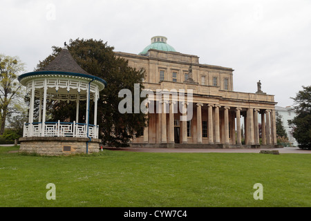 Musikpavillon & die beeindruckende Regency Architektur der Pittville Pump Room, Pittville Park, Cheltenham, Gloucestershire, UK. Stockfoto