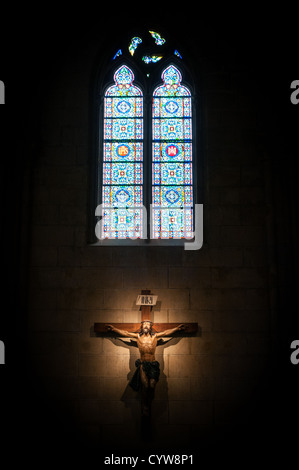 Kruzifix an der Wand im Rampenlicht in alten dunklen Kirche oder Kathedrale. Jesus Christus am Kreuz auf Kontrast mit großen hell gefärbt Stockfoto
