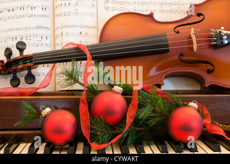 Eine Geige, Noten und Weihnachten Weihnachtsschmuck sitzen auf ein altes Klavier in Erwartung des unterhaltsamen Urlaub. Stockfoto