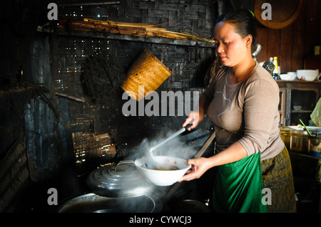 LUANG NAMTHA, Laos — Eine lokale Köchin bereitet in ihrer traditionellen Küche in Luang Namtha, Laos, eine Schüssel Pho (Nudelsuppe) zu. Die Bambuswände hinter ihr sind von jahrelangem Rauch aus dem Holzofen verdunkelt, was die authentischen Kochmethoden veranschaulicht, die noch immer im ländlichen Laos herrschen. Stockfoto