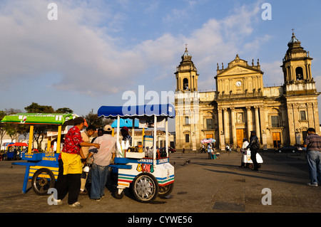 GUATEMALA CITY, Guatemala – die neoklassizistische Catedral Metropolitana dominiert die Ostseite des Parque Central in Guatemala City. Die zwei Glockentürme der Kathedrale ragen über die umliegenden Gebäude, während auf dem belebten Platz vor dem prunkvollen Brunnen und den Einheimischen die Mischung aus kolonialem Erbe und modernem urbanem Leben veranschaulicht. Stockfoto