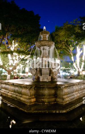 Parque Central Fountain Antigua Guatemala // ANTIGUA GUATEMALA, Guatemala — der zentrale Brunnen im Parque Central in Antigua Guatemala bei Nacht. Antigua Guatemala ist berühmt für seine gut erhaltene spanische Barockarchitektur sowie eine Reihe von Erdbebenruinen und gehört zum UNESCO-Weltkulturerbe und ehemalige Hauptstadt Guatemalas. Stockfoto