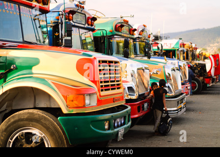 Hühnerbusse Antigua Guatemala | ANTIGUA GUATEMALA, Guatemala — Bunt bemalte Hühnerbusse säumen eine Straße in Antigua Guatemala. Diese umgebauten amerikanischen Schulbusse, geschmückt mit lebhaften Designs und Chromzubehör, stehen bereit, um Einheimische und abenteuerlustige Touristen zu transportieren, und verkörpern Guatemalas lebendige Transportkultur vor dem Hintergrund kolonialer Architektur. Stockfoto