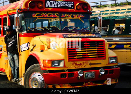 Hühnerbus Antigua Guatemala | ANTIGUA GUATEMALA, Guatemala — Bunt bemalte Hühnerbusse säumen eine Straße in Antigua Guatemala. Diese umgebauten amerikanischen Schulbusse, geschmückt mit lebhaften Designs und Chrom-Accessoires, stehen bereit, um Einheimische und abenteuerlustige Touristen zu transportieren, und verkörpern die lebendige Transportkultur Guatemaltecas vor dem Hintergrund kolonialer Architektur. Stockfoto