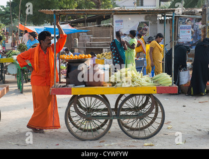 Indischer Mann Straßenhändler verkaufen gekocht Maiskolben auf einem Straßenmarkt. Puttaparthi, Andhra Pradesh, Indien Stockfoto