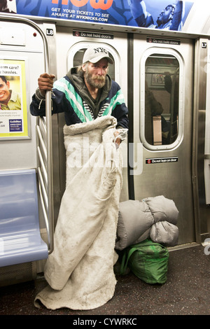 Obdachlosen Mann mit Parka & Decke steht mit Schlafsack neben seinem sauber gebündelt Eigentum auf New Yorker U-Bahn R Zug Manhattan Stockfoto