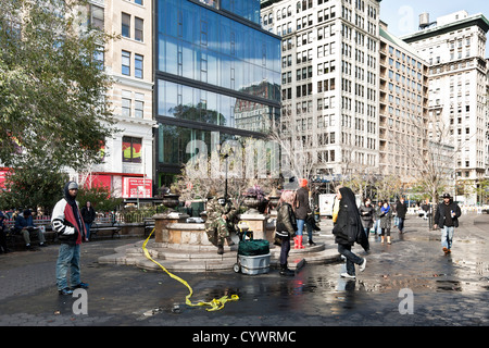 Menschen genießen die warme Herbstsonne in Union Square Manhattan als helle Rinde Schnee links von Wintersturm auf Asphalt schmilzt Stockfoto