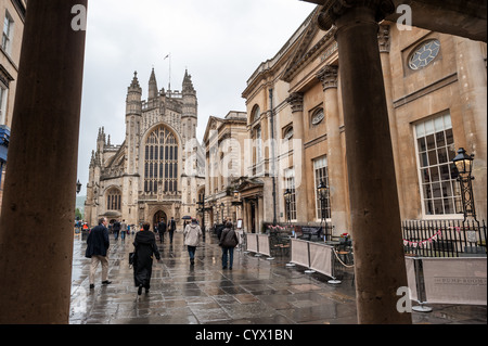 BATH, England – Besucher treffen sich an einem regnerischen Tag im Zentrum von Bath vor dem Eingang zu den historischen römischen Bädern. Der antike römische Badekomplex, der um natürliche heiße Quellen gebaut wurde, geht auf etwa 70 n. Chr. zurück und ist eine der am besten erhaltenen antiken römischen Stätten in Nordeuropa. Im Hintergrund steht die imposante Westfront der Bath Abbey, eine gotische Kirche, die Anfang des 16. Jahrhunderts fertiggestellt wurde. Sowohl die Römischen Bäder als auch die Abtei Bath sind wichtige Wahrzeichen in der UNESCO-Weltkulturerbe-Stadt Bath, die für ihre unverwechselbare georgianische Architektur und gut erhaltene römische Überreste bekannt ist. Stockfoto