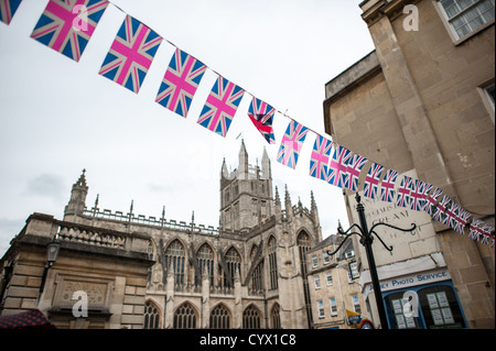 Eine Reihe von Anschluß-Markierungsfahne Wimpel läuft über im Vordergrund, Bath Abbey im Hintergrund im Zentrum von Bath, Somerset, Vereinigtes Königreich. Stockfoto