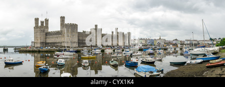 Caernarfon Castle Exterior / CAERNARFON, Vereinigtes Königreich — Ein Panoramablick auf das Äußere von Caernarfon Castle im Nordwesten von Wales. Auf dem Gelände befand sich eine normannische Motte mit Vorburg, die um 1073–93 datiert wurde, bevor König Eduard I. im Sommer 1283 den Bau des heutigen Festungspalastes anordnete, wobei der Bau unter der Leitung des Meisters mason James of St George zeitweise bis etwa 1330 fortgesetzt wurde. Die Burg verfügt über sieben markante polygonale Türme und ein gebändertes Mauerwerk, das an die kaiserlichen Mauern von Konstantinopel erinnern soll, was sie zum architektonisch symbolischsten Waliser Eduards I. macht Stockfoto