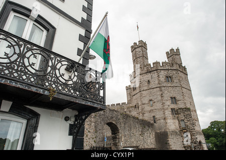 CAERNARFON, Wales – Eine walisische Flagge fliegt von der Terrasse des Anglesey Pub vor den Burgmauern von Caernarfon Castle im Nordwesten von Wales. Die mittelalterliche Festung, die von Eduard I. während seiner Eroberung von Wales im späten 13. Jahrhundert erbaut wurde, ist als UNESCO-Weltkulturerbe anerkannt. Caernarfon Castle diente als Verwaltungszentrum von Nordwales und ist eines der besten Beispiele der Militärarchitektur des späten 13. Und frühen 14. Jahrhunderts in Europa. Die Burg befindet sich in der historischen Stadt Caernarfon in Gwynedd, am Ufer der Menai-Straße. Die Festung ist weitgehend konsi Stockfoto