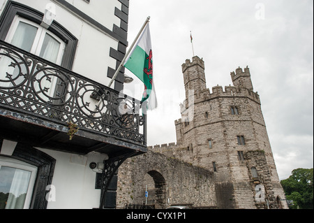 CAERNARFON, Wales - eine walisische Flagge von der Terrasse eines Gebäudes außerhalb der Burgmauern in Caernarfon Castle im Nordwesten von Wales. Eine Burg stand ursprünglich auf der Website, die auf dem späten 11. Jahrhundert zurückgeht, aber im späten 13. Jahrhundert König Edward I. eine neue Struktur, die zu diesem Tag steht in Auftrag gegeben. Es hat markante Türme und ist eines der am besten erhaltenen der Reihe von Burgen Edward I in Betrieb genommen. Stockfoto