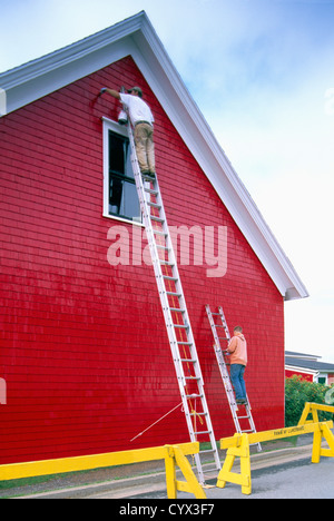 Maler stehen auf Leitern, Malerei helle rote Farbe auf äußere Wand Holz Abstellgleis der ein Lagergebäude Stockfoto