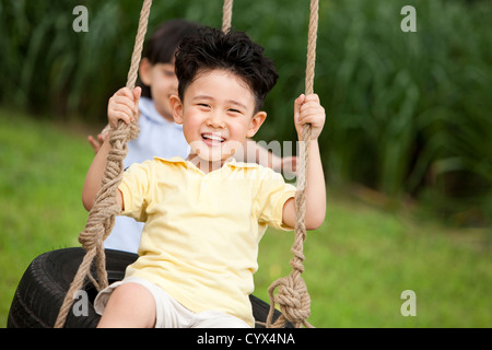 Begeistert junge spielt auf einer Schaukel mit kleinen Mädchen hinter Stockfoto