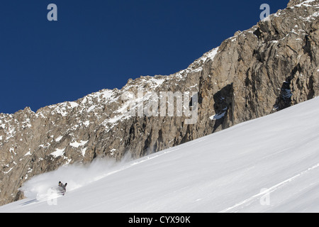 weiblichen Snowboarder wirft frischen Pulverschnee bei der Herstellung einer Wendung mit Bergen im Hintergrund Stockfoto