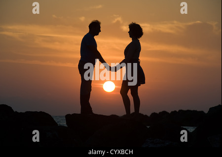 Ein paar bei Sonnenuntergang auf einem Pier Hand in Hand und auf der Suche zueinander Stockfoto