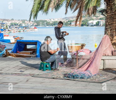 Fischer reparieren Fischernetze unter einem Baum am Rand des Wassers in Foca, Türkei. Stockfoto