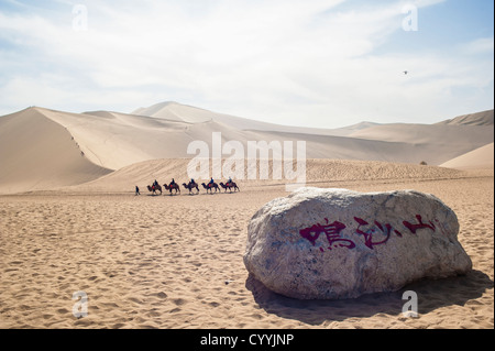 Eine Gruppe von Touristen auf Kamelen Fuß durch die Sanddünen in Dunhuang Stockfoto