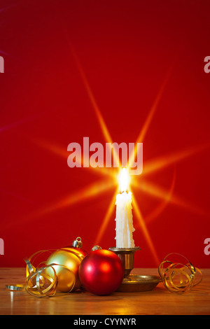 Eine brennende Kerze in Messing Halterung mit Weihnachtsschmuck und rotem Stern Filter verwendet während der Aufnahme für die Flamme Stockfoto