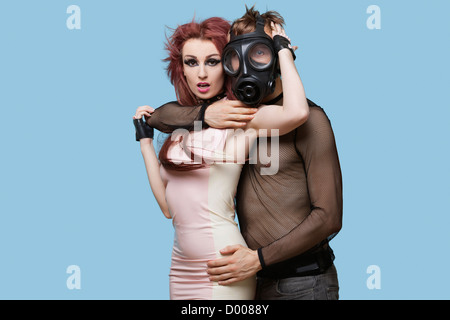 Porträt des jungen Mannes mit Gasmaske umarmt funky Frau auf blauem Hintergrund Stockfoto