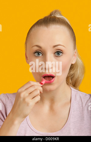 Porträt der schönen jungen Frau Auftragen von Lippenstift auf gelbem Hintergrund Stockfoto