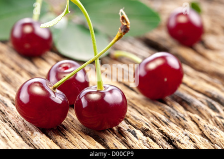 Kirschen mit Blättern auf einem alten Holztisch. Stockfoto