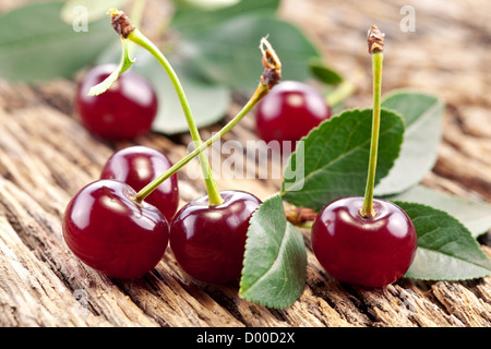 Kirschen mit Blättern auf einem alten Holztisch. Stockfoto