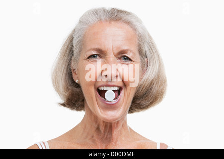 Portrait von senior Frau mit Pille zwischen den Zähnen vor weißem Hintergrund Stockfoto