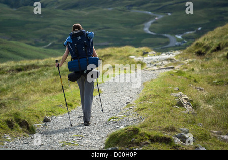 Eine Frau Wanderer zu Fuß entlang einer langen steinernen Pfad mit einem großen Rucksack im Lake District. Stockfoto