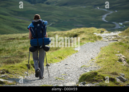 Eine Frau Wanderer zu Fuß entlang einer langen steinernen Pfad mit einem großen Rucksack im Lake District. Stockfoto