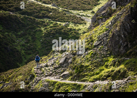 Eine Frau Wanderer zu Fuß einen Stein Weg mit einem großen Rucksack im Lake District. Stockfoto