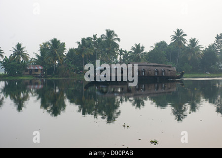 Tourist-Reisbarke vorbei Reflexionen auf der West Coast Canal (National Wasserstraße Nr. 3) bei Sonnenaufgang, Kanjippadom, in der Nähe von Alappuzha (Alleppey), Kerala, Indien Stockfoto