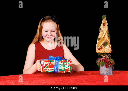 Junge schöne Mädchen mit langen Haaren sitzen Tisch mit Weihnachtsgeschenk - Tisch fallenden roten Tischdecke Stockfoto