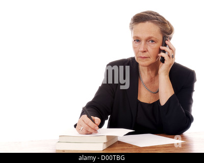 Reife Frau sitzen Tabelle in Handy sprechen und Schreiben von Notizen auf weißem Hintergrund Stockfoto