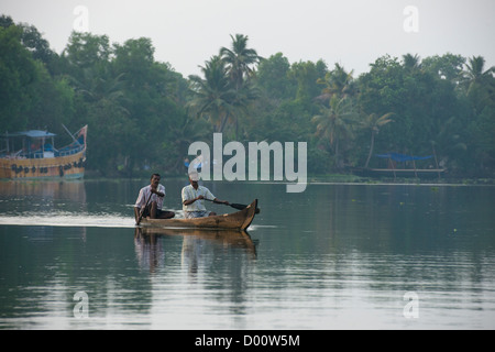 Zwei Männer, eine kleinere Kanu rudern, vorbei an großen bunten Fischerboote auf der West Coast Canal (National Wasserstraße Nr. 3), Kanjippadom, in der Nähe von Alappuzha (Alleppey), Kerala, Indien Stockfoto